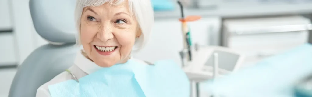 Woman smiling in a dental chair after receiving fixed dentures.