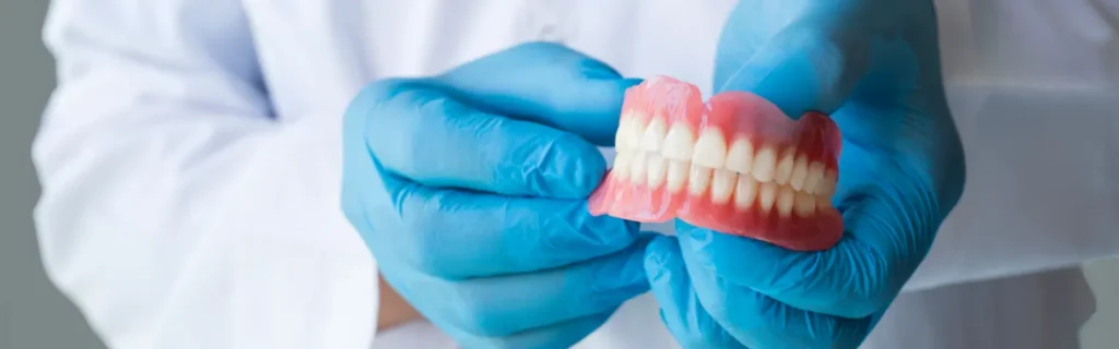 Dentist holding a set of dentures with blue gloves