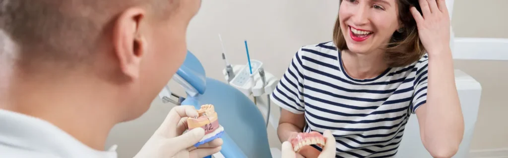 Dentist showing a dental implant model to a smiling patient in a clinic.